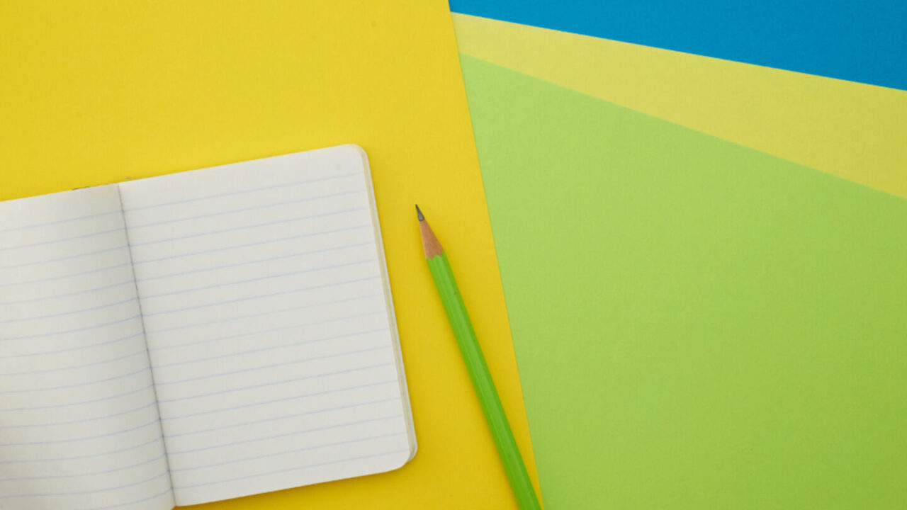 Blocco note aperto e matita su fondo colorato, articoli tipici della regalistica promozionale